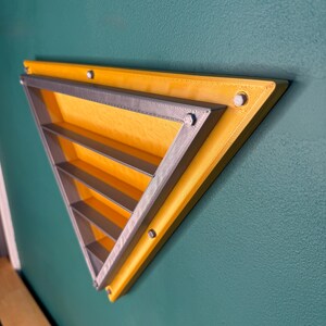 May include: A yellow and gray triangular wall shelf with multiple horizontal shelves. The shelf is mounted on a teal wall with silver colored screws. The shelf is a modern design.