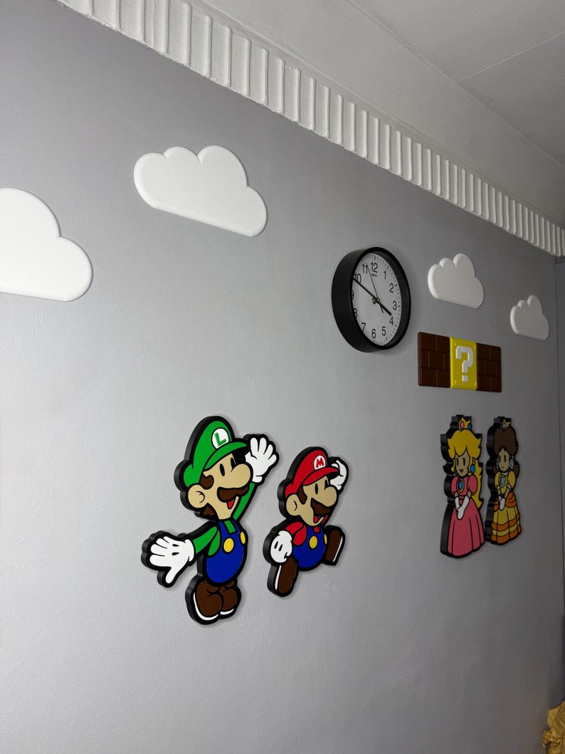 Op de afbeelding: Muurdecoratie met personages uit het Super Mario Bros. videospel. Inclusief Mario, Luigi, Princess Peach en Daisy, samen met witte wolkuitsparingen, een vraagtekenblok en een zwarte analoge klok.
