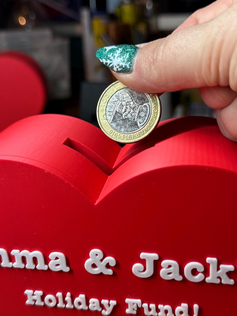 Hand placing a coin in a Love heart-shaped piggy bank, ideal for saving coins, Valentine’s Day gifts, or romantic decor. A unique 3D-printed coin bank for kids or couples, perfect as a gift, decorative piece, or practical savings tool.