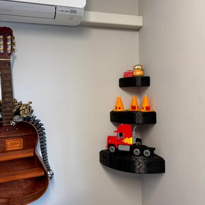 May include: Three-tiered corner shelf unit made from black tires. The top shelf holds two toy cars. The middle shelf has three orange traffic cones. The bottom shelf displays a red toy semi-truck.
