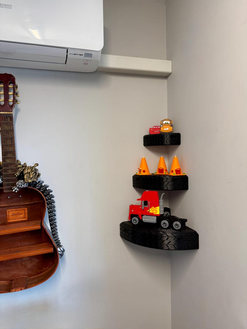 May include: Three-tiered corner shelf unit made from black tires. The top shelf holds two toy cars. The middle shelf has three orange traffic cones. The bottom shelf displays a red toy semi-truck.