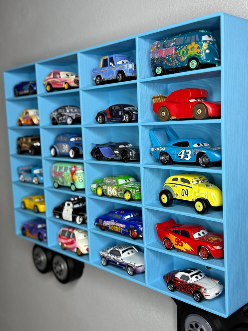 May include: A blue, wall-mounted display shelf filled with various toy cars. The shelf has multiple compartments, each holding a different car model. The cars are in various colors, including red, blue, yellow, and green. The shelf is designed to resemble a truck.
