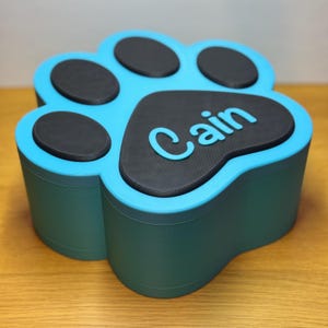 Paw print-shaped pet memorial box with personalised name on the lid. Holds up to 1300ml, ideal for pet ashes or keepsakes. Customisable colours available. Secure magnetic closure. Thoughtful pet loss gift. Designed for home display.