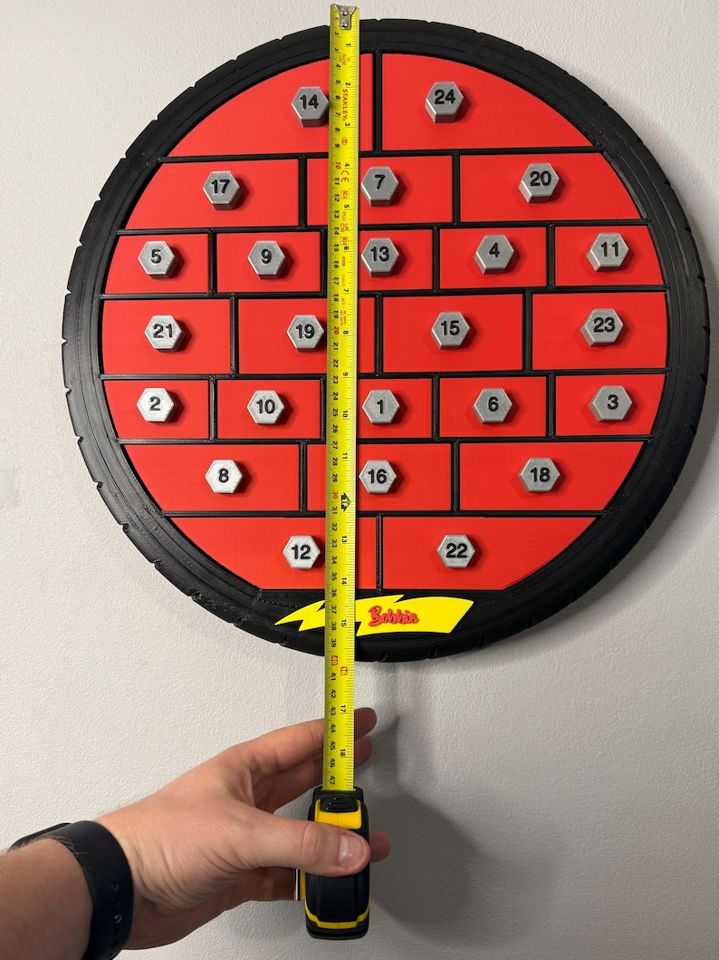 May include: A red and black advent calendar with 24 numbered compartments. The calendar is circular, with a tire-like outer rim. A yellow measuring tape shows the calendar is approximately 18 inches tall.