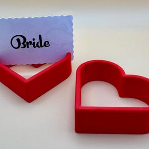 Heart-shaped wedding place card holders in vibrant red, perfect for elegant table settings. Displaying a “Bride” card, this durable design adds charm to weddings, bridal showers, and romantic events. for custom wedding décor and table name displays.