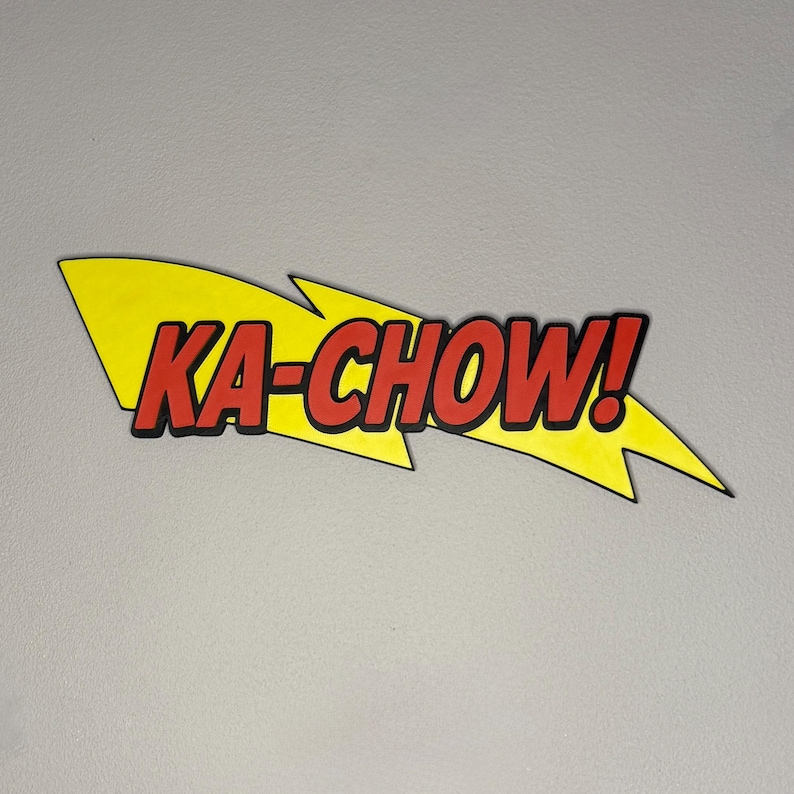 May include: A yellow lightning bolt shape with the words "KA-CHOW!" in red letters with a black outline. The exclamation point is included. The design is against a light gray background.