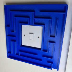 A 3D-printed, decorative light switch cover with a maze-like design. The intricate pattern adds a unique and playful touch to any room, making it both functional and visually appealing for various settings.