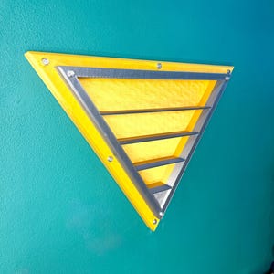 May include: A yellow triangular wall shelf with a silver trim and horizontal shelves. The shelf is mounted on a teal wall. The shelf is approximately 12 inches wide.