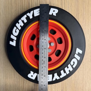 May include: A black and red decorative wheel with the text "LIGHTYEAR" in white. The wheel is approximately 9 inches in diameter, with a yellow stripe between the red center and black tire.