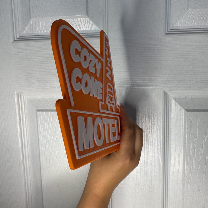 以下が含まれることがあります： レトロなスタイルの「Cozy Cone Motel」という文字が書かれたオレンジと白の看板