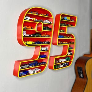 May include: Red and yellow wall-mounted display shelves shaped like the number 95, filled with miniature toy cars. The shelves are red with yellow trim, and the cars are various colors and styles.