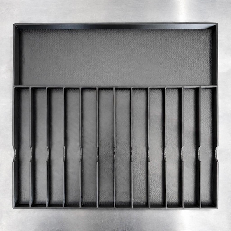 May include: A dark gray organizer tray with a rectangular shape. The tray has a large upper compartment and a lower section divided into 12 narrow vertical slots. The surface has a textured appearance.