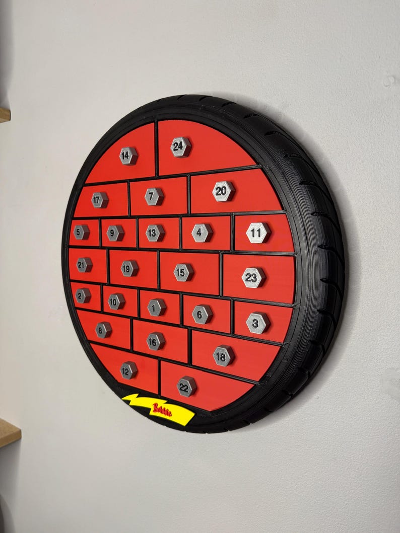 May include: A round, red advent calendar with a black tire-like frame. It features 24 numbered compartments with silver-colored, hexagonal knobs. The word "Battle" is visible on a yellow banner.