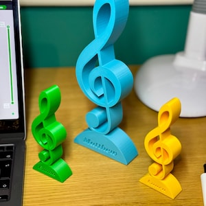Three personalised treble clef trophies in blue, green, and yellow, each engraved with a custom name. A stylish musician gift for teachers, students, and performers. Available in various sizes, ideal for music lovers’ desks or shelves.