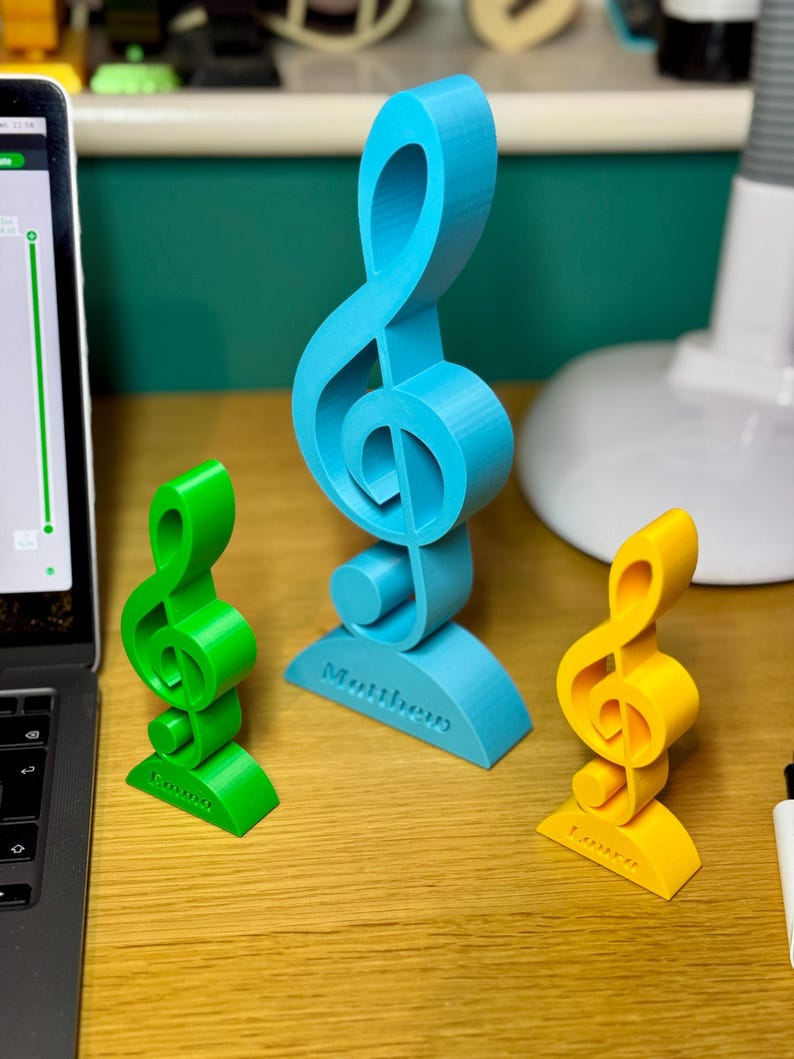 Three personalised treble clef trophies in blue, green, and yellow, each engraved with a custom name. A stylish musician gift for teachers, students, and performers. Available in various sizes, ideal for music lovers’ desks or shelves.