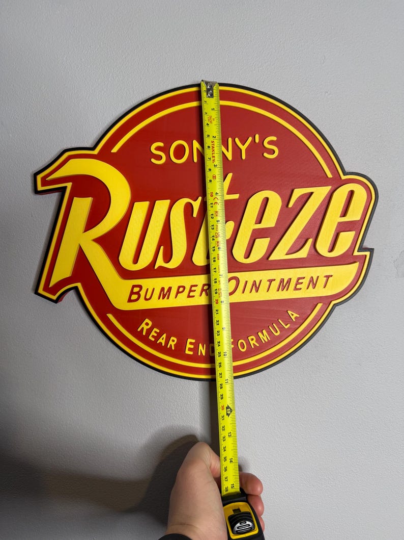Puede incluir: Un letrero redondo rojo y amarillo con el texto "SONNY'S RUST-EZE BUMPER OINTMENT REAR END FORMULA". El letrero mide aproximadamente 94 cm de alto. Se sostiene una cinta m&eacute;trica amarilla contra el letrero.