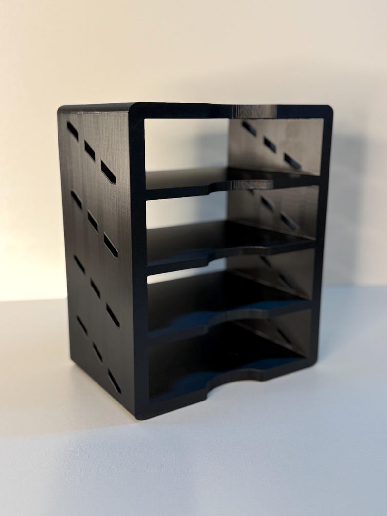 May include: A black, four-tiered shelf unit with a rectangular shape. The sides feature diagonal cut-out designs. The shelves are evenly spaced, and the unit has a curved bottom edge. The unit is made of a solid, matte black material.