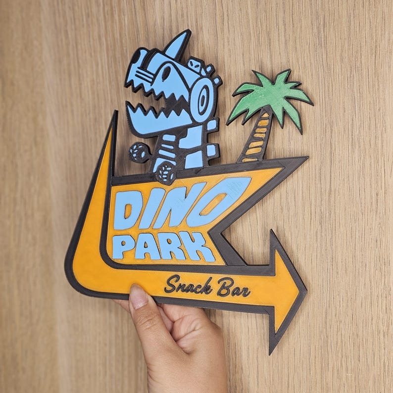 May include: A wooden Dino Park sign featuring a cartoon dinosaur and palm tree. The sign is yellow and black with blue text that reads "DINO PARK Snack Bar". The arrow points to the right.