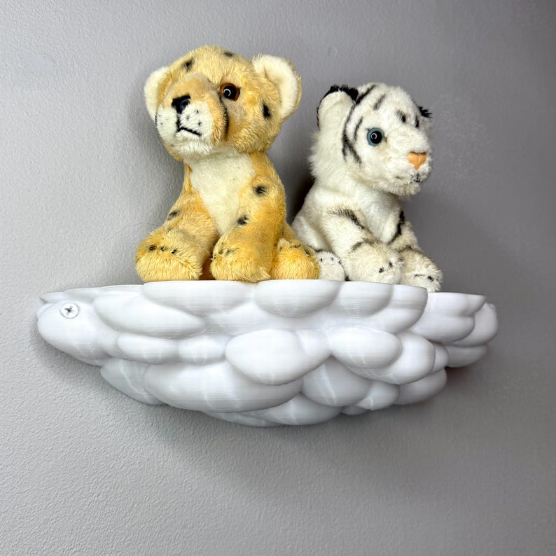 May include: A white cloud-shaped shelf holds two plush toy animals. One is a yellow cheetah cub with black spots, and the other is a white tiger cub with black stripes. The shelf is mounted on a gray wall.