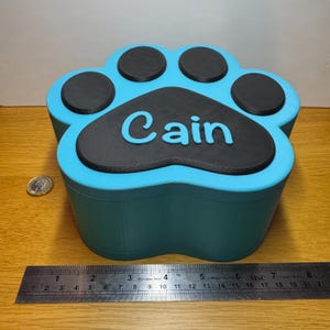 Large paw print pet memorial box with personalised name. Holds up to 1300ml, suitable for dogs up to 35kg. Magnetic lid for secure closure. Custom colours available. Thoughtful urn alternative for pet ashes or keepsakes. Durable 3D-printed design.