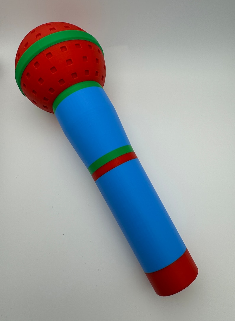 A 3D-printed, colorful plastic microphone prop held in a hand. This vibrant and durable design is perfect for photo booth props, party accessories, or as a fun kids' toy, available in various color combinations.