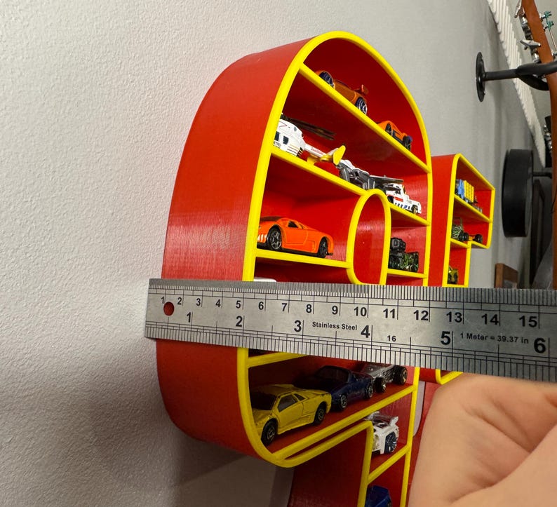 May include: A red and yellow shelf in the shape of the word "HOT" is filled with miniature toy cars. The shelf is approximately 5 inches wide. The cars are various colors and styles.