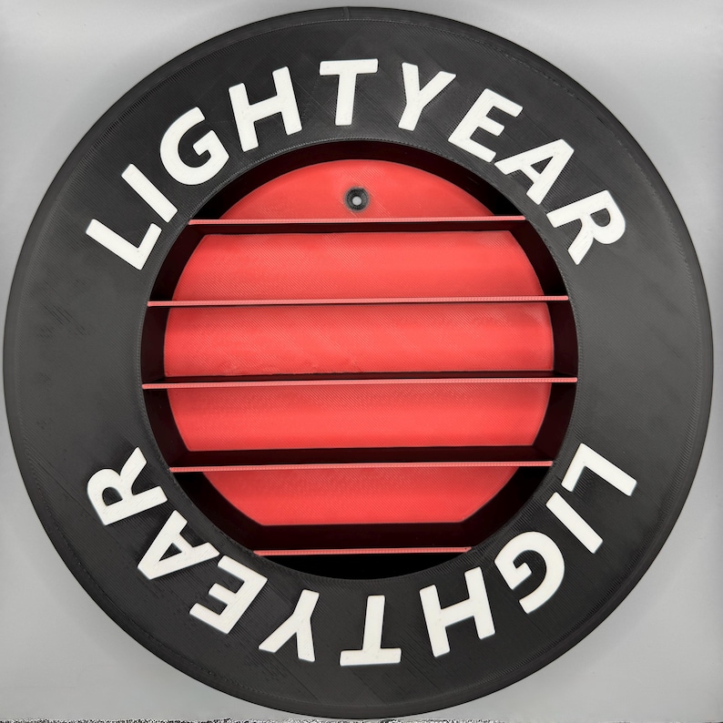 May include: A circular black object with the word "LIGHTYEAR" in white lettering. The center features a red, slatted design. A small, dark screw is visible at the top. The overall design is reminiscent of a spaceship element.