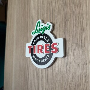 May include: A white, red, and black sign with the text "Luigi's Casa Della Tires Quality Service". The sign has a green, stylized "Luigi's" logo above the circular text.