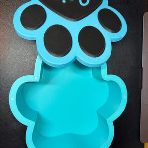 Paw print-shaped pet memorial box with personalised name on the lid. Holds up to 1300ml, ideal for pet ashes or keepsakes. Customisable colours available. Secure magnetic closure. Thoughtful gift for dog or cat owners. Designed for home display.