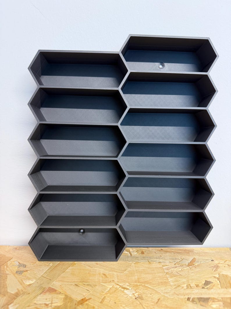 May include: A dark gray wall-mounted storage unit featuring a modular honeycomb design with ten hexagonal compartments arranged in two vertical columns. The structure is made of a matte material and includes two visible circular mounting holes.