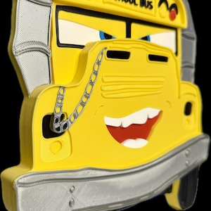 K&ouml;nnte beinhalten: Ein gelber Schulbus mit einem l&auml;chelnden Gesicht, blauen Augen und dem Schriftzug "SCHOOL BUS" oben. Der Bus hat eine silberne Sto&szlig;stange und schwarze Reifen. Eine silberne Kette h&auml;ngt von der Vorderseite. Der Bus ist ein 3D-Druck-Design.