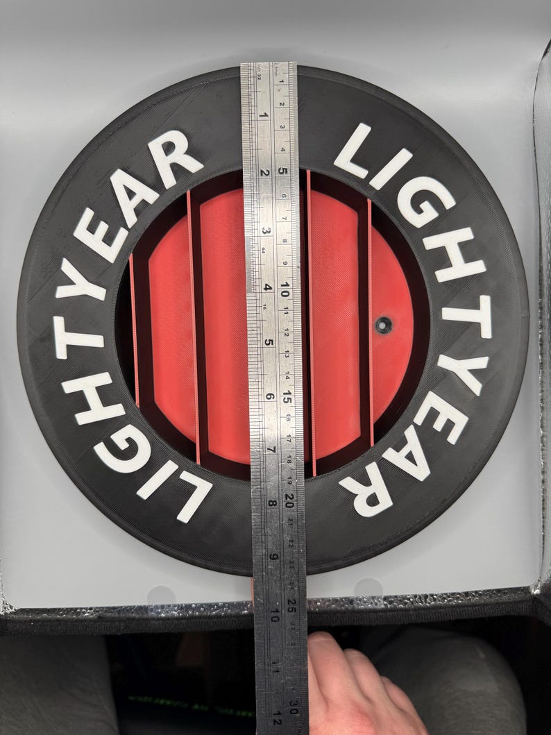 May include: A black and red circular object with the text "LIGHTYEAR" in white. The object has a series of red vertical bars in the center. A ruler is placed on the object, measuring approximately 12 inches.