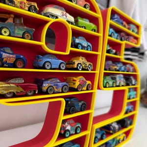 May include: A red and yellow display shelf shaped like the number 97, filled with toy cars of various colors and designs. The shelf has multiple levels to hold the toy cars. The cars are miniature replicas of different car models.