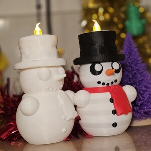 Adorable 3D-printed snowman tealight holders in white and multicolour, featuring festive designs with hats, scarves, and LED tealights. Perfect as Christmas decorations or gifts, displayed on a table with holiday-themed backdrops.