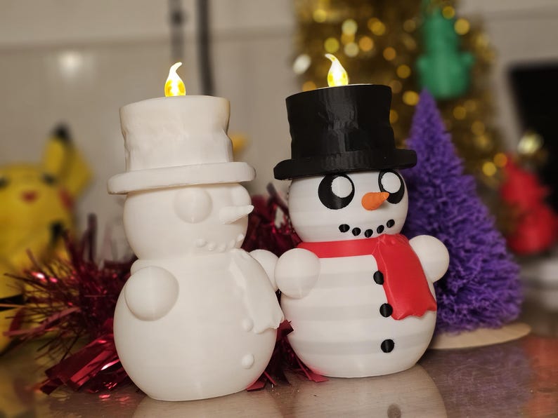 Adorable 3D-printed snowman tealight holders in white and multicolour, featuring festive designs with hats, scarves, and LED tealights. Perfect as Christmas decorations or gifts, displayed on a table with holiday-themed backdrops.