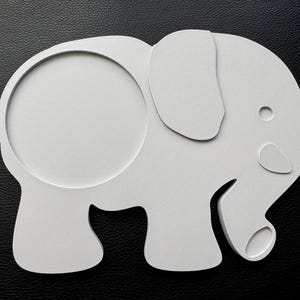 3D-printed white PLA elephant-shaped coaster with a 90mm circular hole, placed on a black leather surface for display.