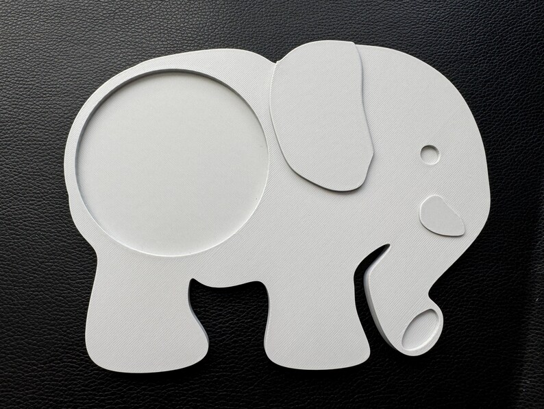 3D-printed white PLA elephant-shaped coaster with a 90mm circular hole, placed on a black leather surface for display.