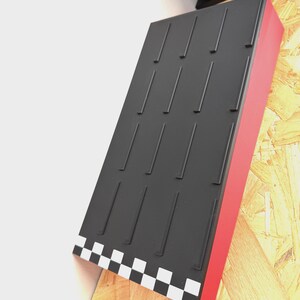 May include: A black display stand with a red side and a checkered pattern at the bottom. The stand has multiple vertical slots and is mounted on a wooden surface.