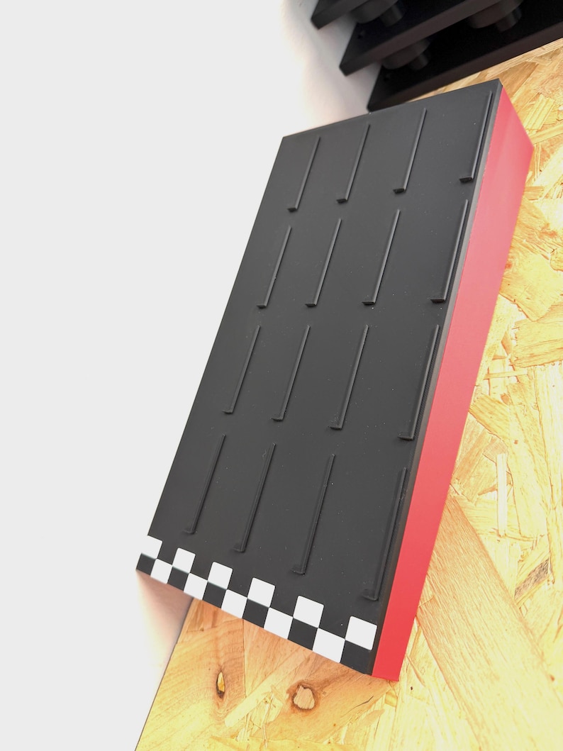 May include: A black display stand with a red side and a checkered pattern at the bottom. The stand has multiple vertical slots and is mounted on a wooden surface.