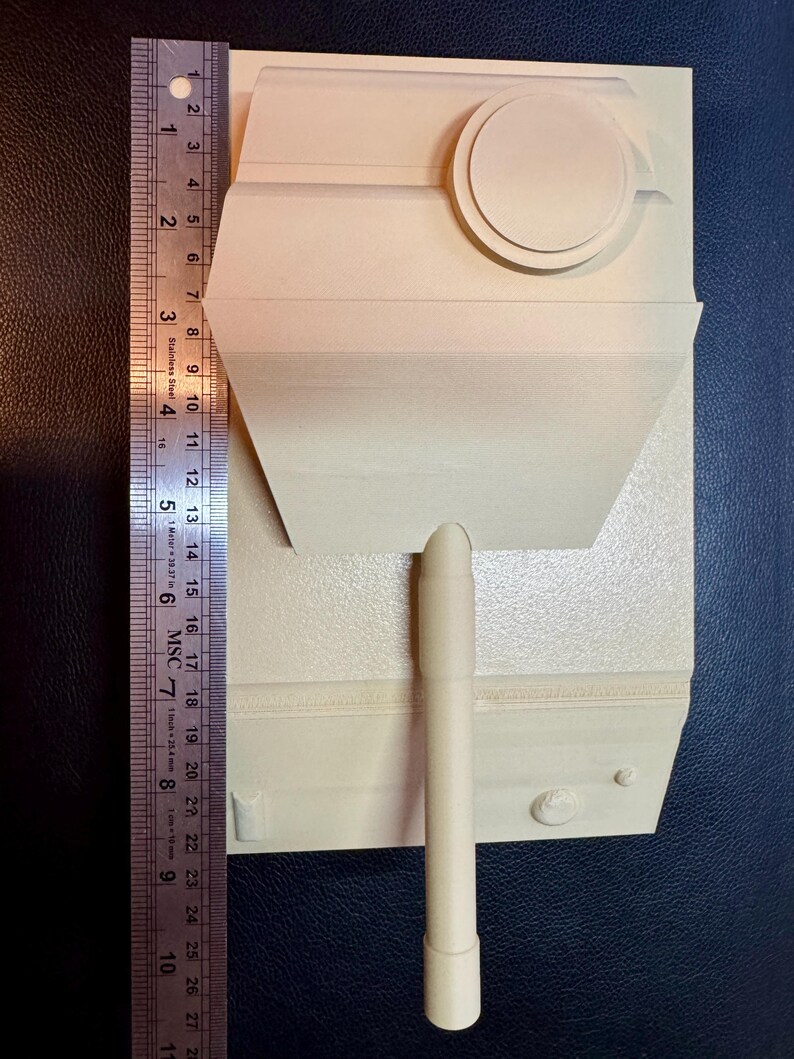 May include: A cream-colored, unpainted plastic model tank turret with a long barrel and a circular hatch. A stainless steel ruler is positioned along the left side, showing the model measures approximately 8.5 inches in total length.