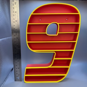 May include: A red and yellow number nine-shaped shelf. The shelf has a red interior with yellow trim and horizontal shelves. The number nine is approximately 10 inches tall and has a hole on the top for hanging.