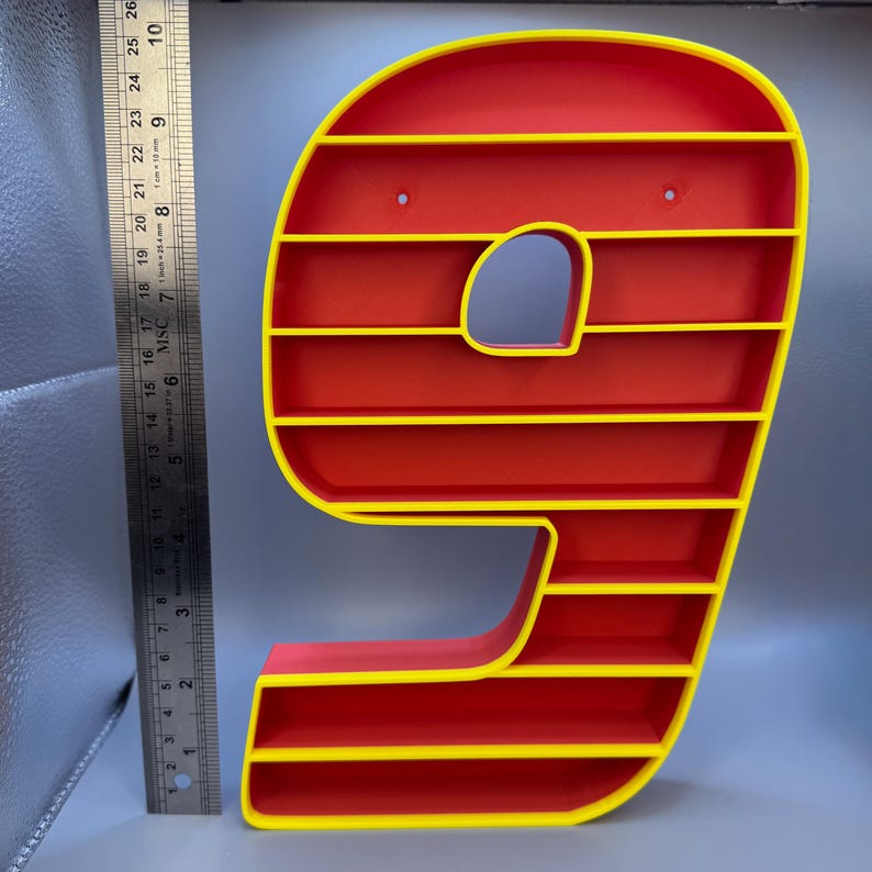 May include: A red and yellow number nine-shaped shelf. The shelf has a red interior with yellow trim and horizontal shelves. The number nine is approximately 10 inches tall and has a hole on the top for hanging.