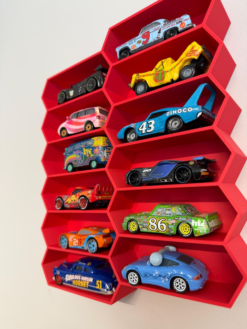 May include: A bright red wall-mounted display shelf with a honeycomb pattern, featuring ten individual hexagonal compartments. Each compartment holds a single die-cast toy car, including various colorful models with racing numbers and graphic designs.
