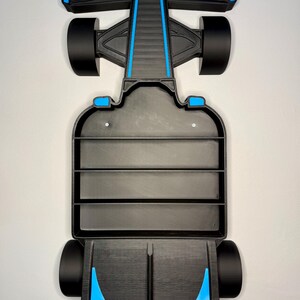 Op de afbeelding: Een zwart en blauw Formule 1 raceauto schap. Het schap heeft een zwarte carrosserie met blauwe accenten op de voor- en achtervleugels en langs het midden. Het schap heeft drie horizontale planken voor display en zwarte wielen.