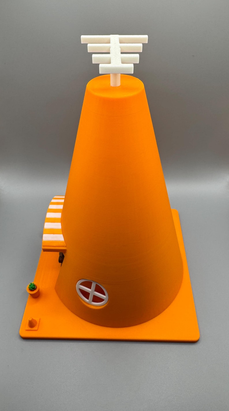Op de afbeelding: Een 3D-geprint oranje verkeerskegelhuis met een wit gestreept luifel, een klein raam en een witte antenne op de top.