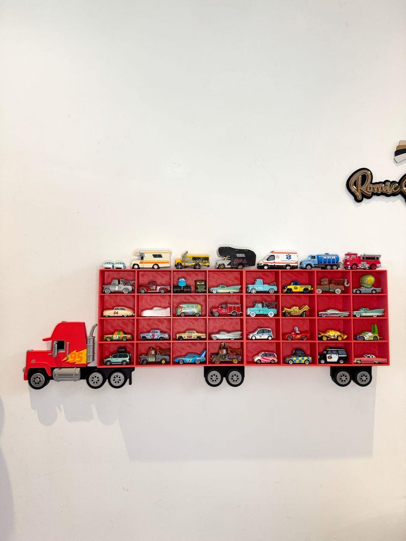 May include: A red truck-shaped shelf filled with various toy cars. The shelf is mounted on a white wall and features a detailed design of a truck with wheels and a trailer. The toy cars are of different colors and styles.