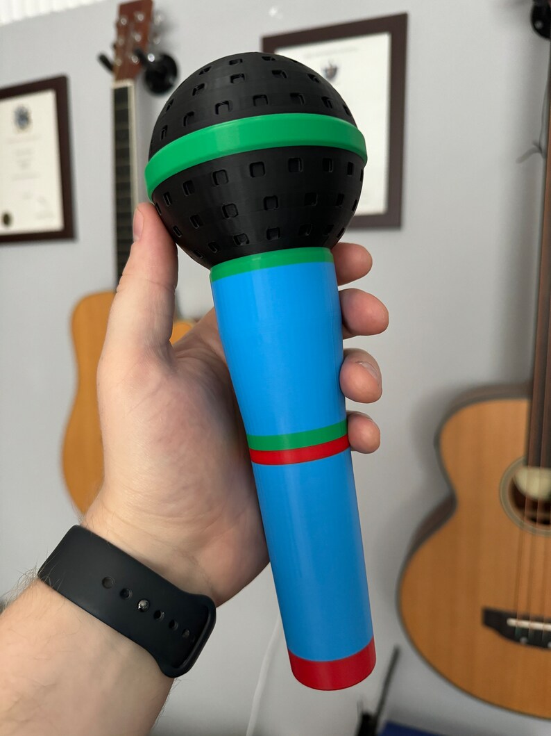 A 3D-printed, colorful plastic microphone prop held in a hand. This vibrant and durable design is perfect for photo booth props, party accessories, or as a fun kids' toy, available in various color combinations.