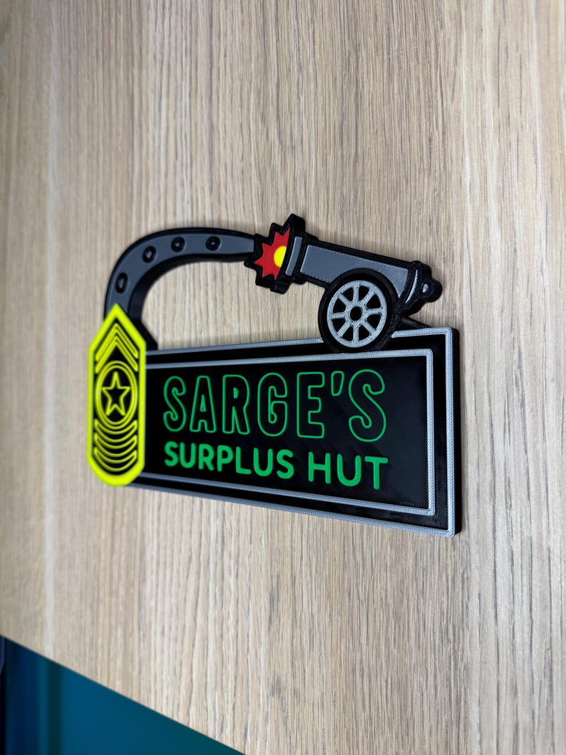 May include: A black and green sign with the text "SARGE'S SURPLUS HUT" in green lettering. The sign features a cartoon cannon firing a red and yellow burst. A yellow and black military insignia is on the left.