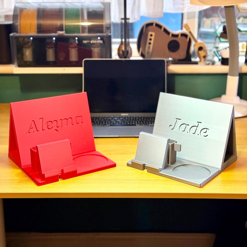 personalised 3D-printed book rest and desk organiser in red & silver, each featuring a custom name. Includes a phone stand, cup holder, and storage for pens or accessories. Ideal for a workspace, bedside table, or study. Available in various colours