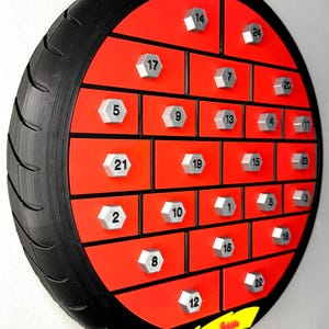 May include: A unique, round advent calendar designed to resemble a tire. The calendar features a red interior with numbered compartments and silver-colored bolt-shaped knobs. The outer rim is black, with tire tread detailing. A yellow arrow points to the word "Soon".